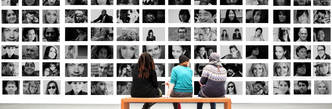 Drei Jugendliche sitzen vor einer Wand mit vielen Porträtfotos.