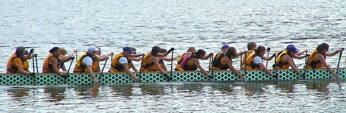 Das Foto zeigt Menschen in einem langen Ruderboot.