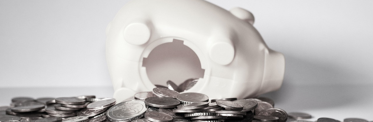 Das Foto zeigt ein kaputtes Sparschwein, vor dem viele Münzen liegen.